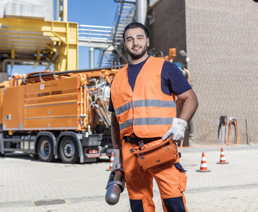 Auszubildender in oranger Arbeitskleidung vor Pumpfahrzeug