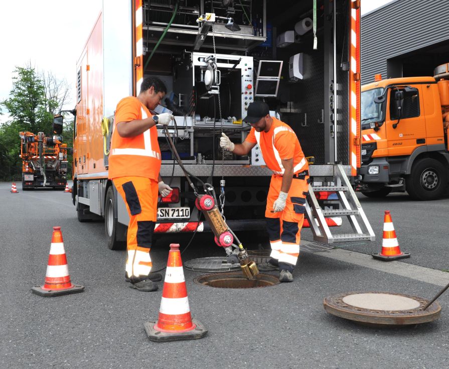 Zwei Arbeiter vor Werkstattfahrzeug an geöffnetem Kanalschacht