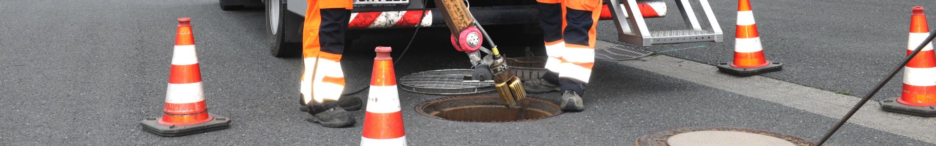 Geöffneter Kanaldeckel vor Fahrzeug mit Spülwerkzeug